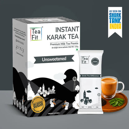 Tea Fit Instant Karak Tea Premium Milk Tea Premix in a white and black box, shown alongside a single sachet, a glass of milk tea, and green tea leaves on a gray background with a Shark Tank India badge.