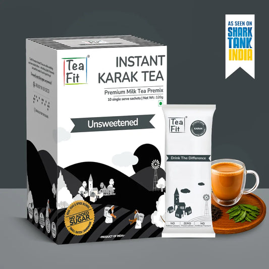 Tea Fit Instant Karak Tea Premium Milk Tea Premix in a white and black box, shown alongside a single sachet, a glass of milk tea, and green tea leaves on a gray background with a Shark Tank India badge.