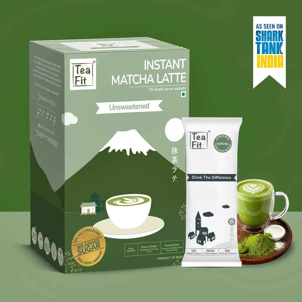 Tea Fit Instant Matcha Latte Unsweetened packaging shown with a single sachet, a cup of matcha latte, and a green powder bowl on a green background. A badge in the top right says 'As seen on Shark Tank India'.