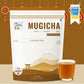 A stand-up pouch of Tea Fit Mugicha loose-leaf tea, shown alongside a clear glass filled with the brewed tea. The packaging is primarily white with brown and gold accents, featuring a minimalist mountain and torii gate illustration.
