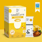 Tea Fit Instant Turmeric Latte Unsweetened product packaging shown with a single sachet, a glass of prepared latte, and turmeric root props on a yellow background. A badge reading 'As seen on Shark Tank India' appears in the top right.