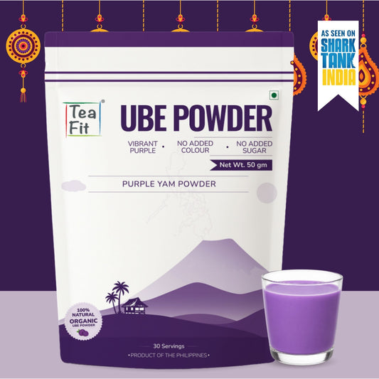 A 50g stand-up pouch of Tea Fit Ube Powder (Purple Yam Powder) shown next to a glass of purple powder, set against a dark purple festive background with hanging ornaments.